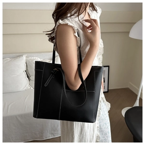 Détail d'un sac cabas noir avec surpiqûres blanches et une boucle en métal doré