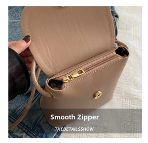 Detail of smooth metal zipper and magnetic snap closure on beige leather bucket bag