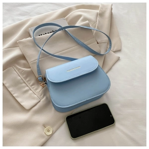Detail of light blue saddle bag on beige blazer featuring golden lettering and smooth texture
