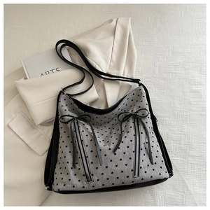 Detail of grey tote bag featuring black heart prints, bow tie decor, and dual zippers