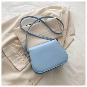 Detail view of a light blue minimalist saddle bag on a beige blazer with gold hardware