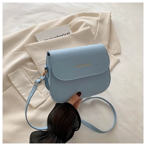 Detail of light blue faux leather saddle bag with gold logo on a cream blazer background