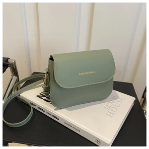 Detail of sage green saddle bag with gold FASHION & BAGS lettering and hardware