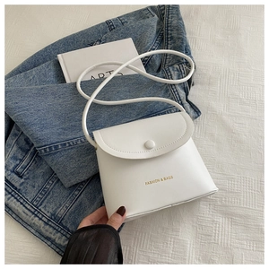 Detail of white PU leather crossbody bag with gold text and button on denim jacket