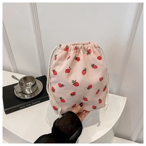 Détail d'un sac à cordon en velours rose avec imprimé fraises tenu par une main