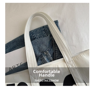 Detail of wide reinforced handles and black lettering on white faux leather tote bag