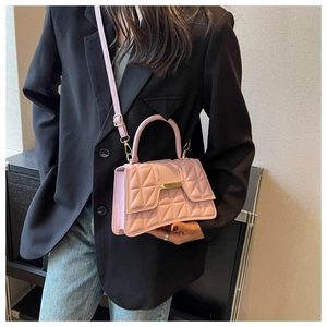 Sac bandoulière matelassé rose avec détails dorés porté par un mannequin en blazer