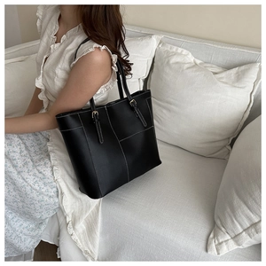 Sac fourre-tout noir chic avec surpiqûres blanches et boucles dorées porté par un mannequin