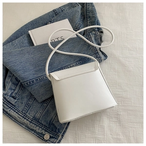 Close-up of minimalist white square crossbody bag on blue denim jacket background