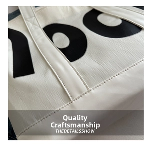 Close-up of white canvas tote bag with black 100 print showing precision stitching