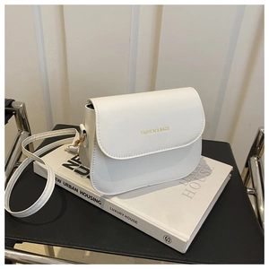 Detail of white leather saddle bag with gold lettering on a stylish book setting