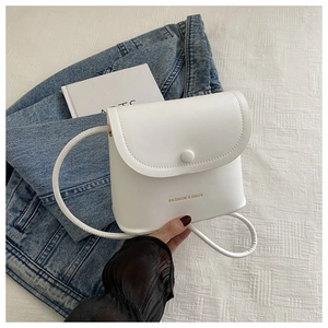 Detail of white minimalist square bag showing the round flap and gold lettering