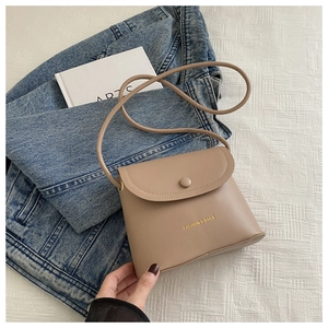 Close-up of a khaki crossbody bucket bag with gold lettering on white fabric