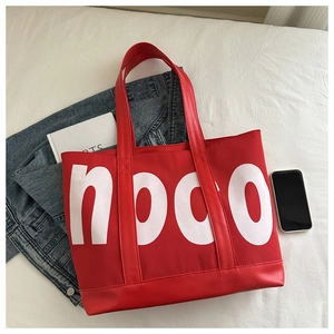 Detail of red tote bag featuring large white noco lettering and wide leather handles