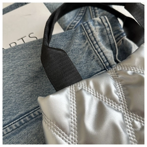 Détail du sac matelassé argenté avec bandoulière noire sur fond en denim et carte