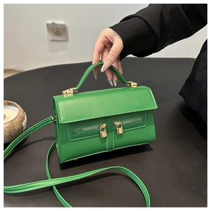 Détail du sac en cuir vert avec deux fermetures éclair dorées et petit pendentif cadenas