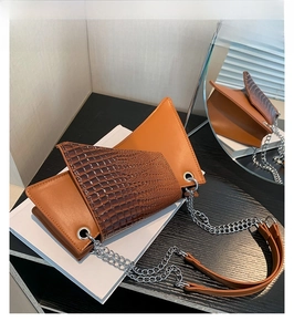 Détail d'un sac à bandoulière marron avec motif croco sur un livre blanc et miroir