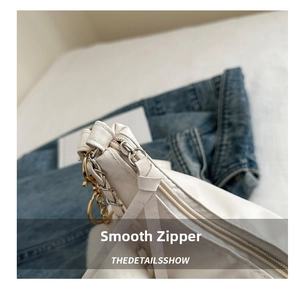 Detailed macro view of smooth gold zipper and white leather strap on a chic tote bag