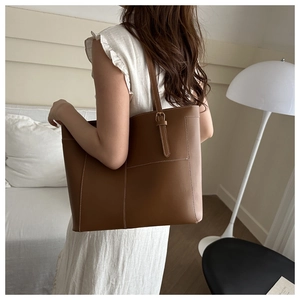 Sac fourre-tout en cuir marron avec surpiqûres blanches et boucles dorées sur un mannequin