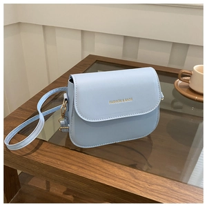Detail of light blue PU leather crossbody bag with golden hardware on a wooden table