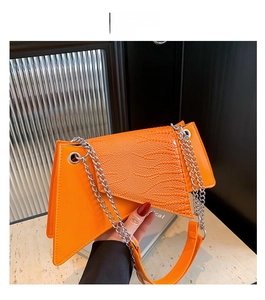 Détail du sac à main orange asymétrique avec texture crocodile et chaîne argentée