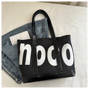 Flat lay of a large black noco tote bag on denim jeans with a minimalist lifestyle vibe