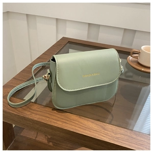 Detail of light green PU leather crossbody bag with gold embossed logo on a wooden table