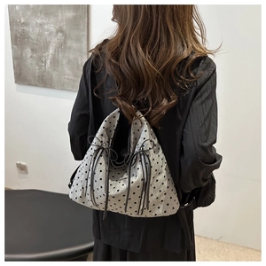 Detail of grey heart print tote bag featuring decorative zippers and black ribbons