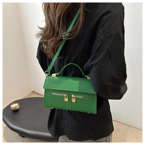 Mannequin portant un sac bandoulière en cuir vert brillant avec fermetures éclair dorées