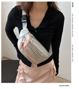 Detail of silver crossbody bag with pink lettering and thick woven zipper pulls on model