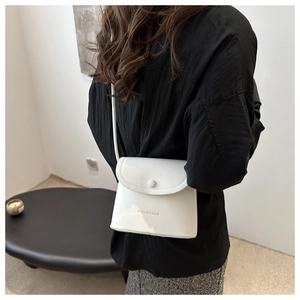 Close-up of white minimalist flap crossbody bag with button closure and printed logo
