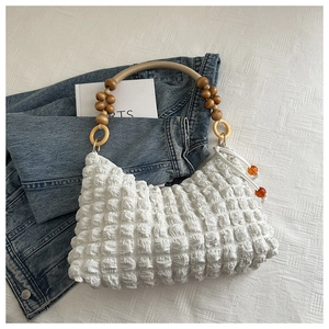 Détail d'un sac à main blanc plissé avec poignée en perles de bois et cordon à perles