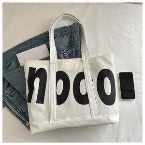 Detailed close-up of white PU leather tote with black nocoi lettering and cross-stitched handles