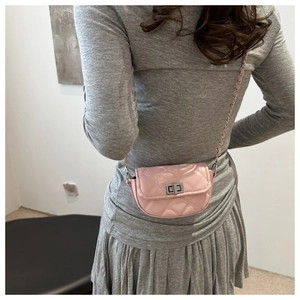 Sac à bandoulière rose matelassé avec chaîne argentée porté sur une robe grise plissée