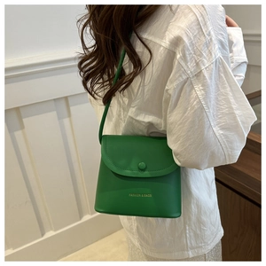 Detail of green minimalist crossbody bucket bag with golden lettering on a model