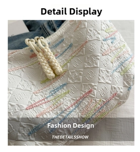 Detailed close-up of quilted white tote fabric with colorful wave embroidery and zipper pull