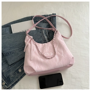 Close-up of pink hobo bag with pleated texture, silver chain, and casual lifestyle props