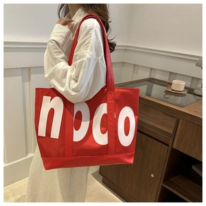 Detail of red canvas tote bag with white noco lettering and shoulder straps