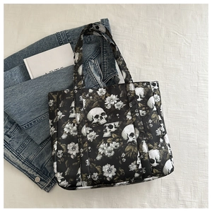 Flat lay of a black skull and floral print tote bag with stylish denim jacket and book