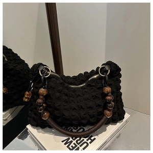 Détail d'un sac noir à texture bulle avec poignée en perles de bois marron