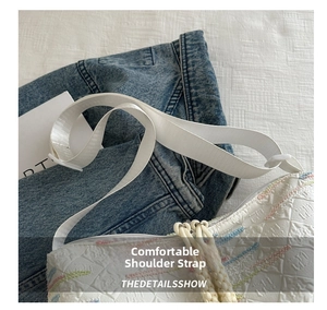 Detailed close-up of wide white shoulder strap and colorful embroidery on canvas tote bag