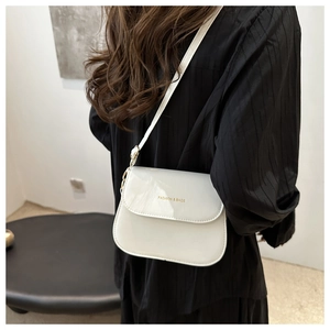 Close-up of white glossy patent leather saddle bag worn over the shoulder by a model