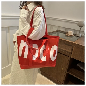 Detail of red oversized tote bag with white lettering print worn on shoulder