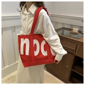 Detail of red oversized nylon tote bag with node logo carried on shoulder by a model