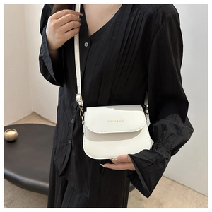 Close-up of minimalist white saddle bag on a model wearing a black pleated dress