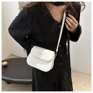 Detail of white saddle bag with gold logo and shoulder strap worn on black outfit