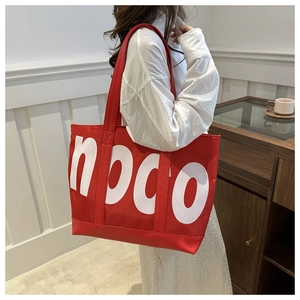 Detailed view of red canvas tote bag with white NOCO print worn by a model