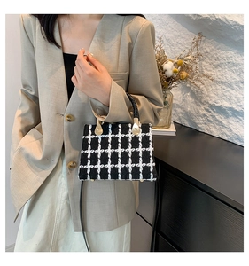 Detail of black and white tweed crossbody bag with golden hardware and woven handle