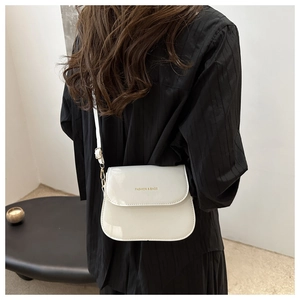 Detail of white glossy saddle bag showing gold logo and adjustable shoulder strap on model