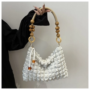 Détail d'un sac à main blanc plissé avec poignée en perles de bois et tissu à bulles
